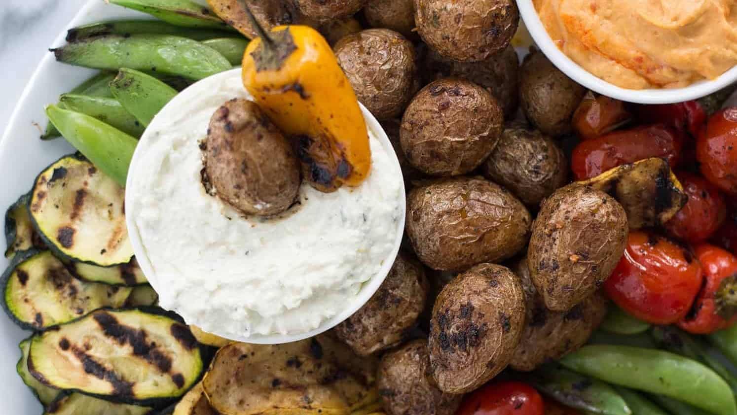 A plate full of grilled veggies with two dip sauces.