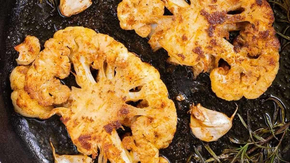 Two cauliflower steaks in a pan.